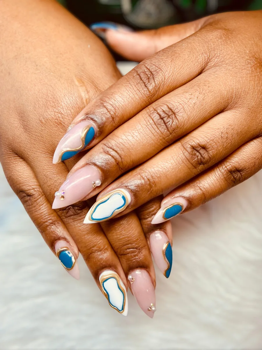 Nude almond nails with blue and white swirls outlined in gold with tiny pearl accents by Hailey Nguyen
