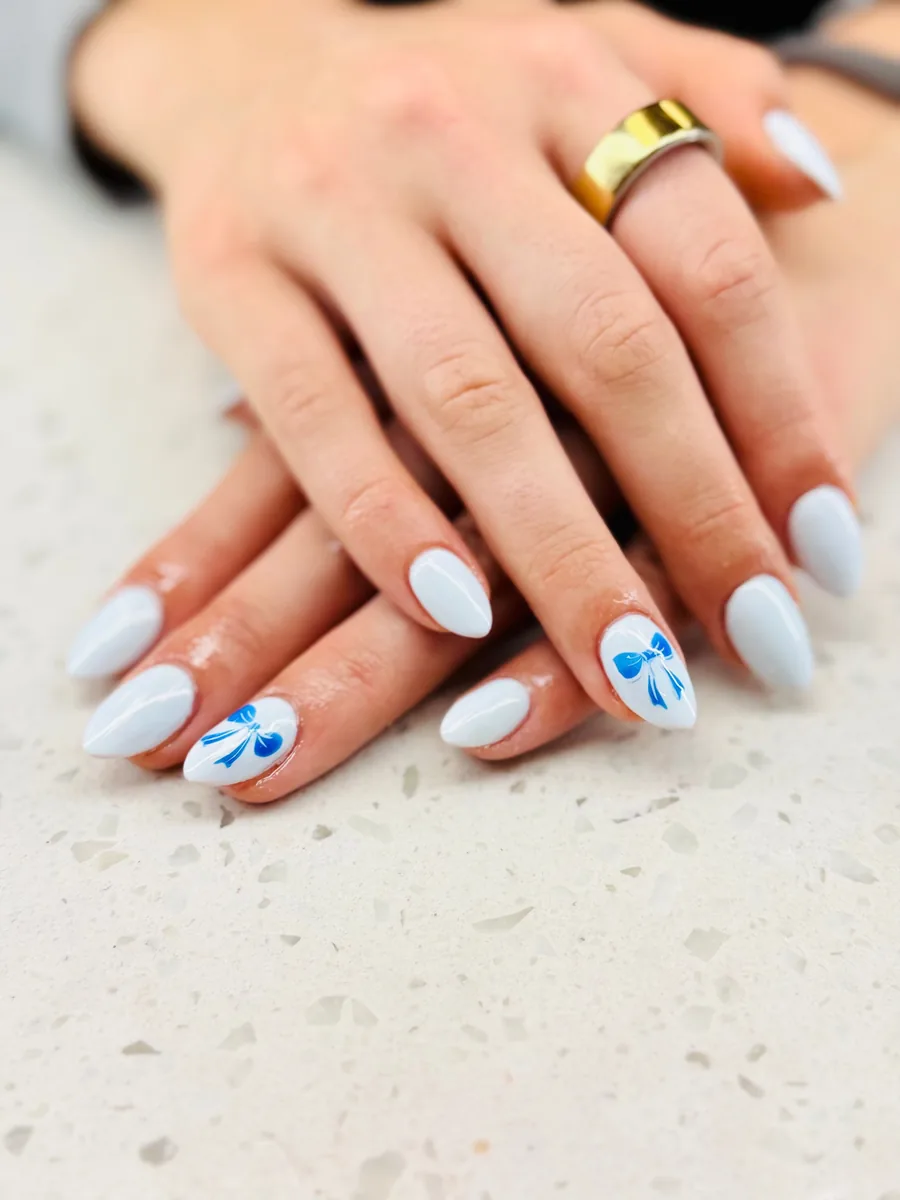 Soft baby blue almond nails with hand painted blue bows by Hailey Nguyen