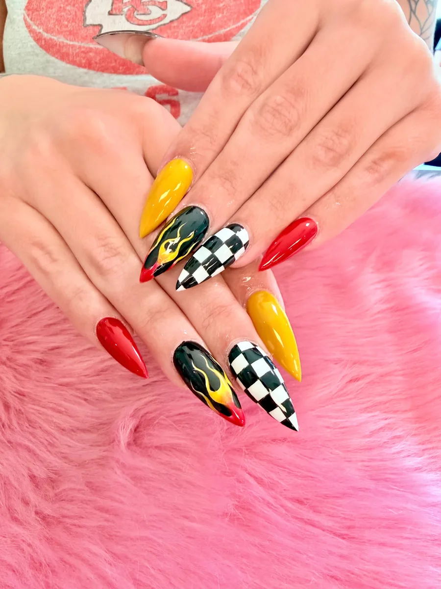 Red and yellow stiletto nails with black flame and checkered flag designs by Hailey Nguyen
